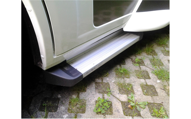 Marchepied replié sur un véhicule blanc garé sur un sol pavé avec de l'herbe