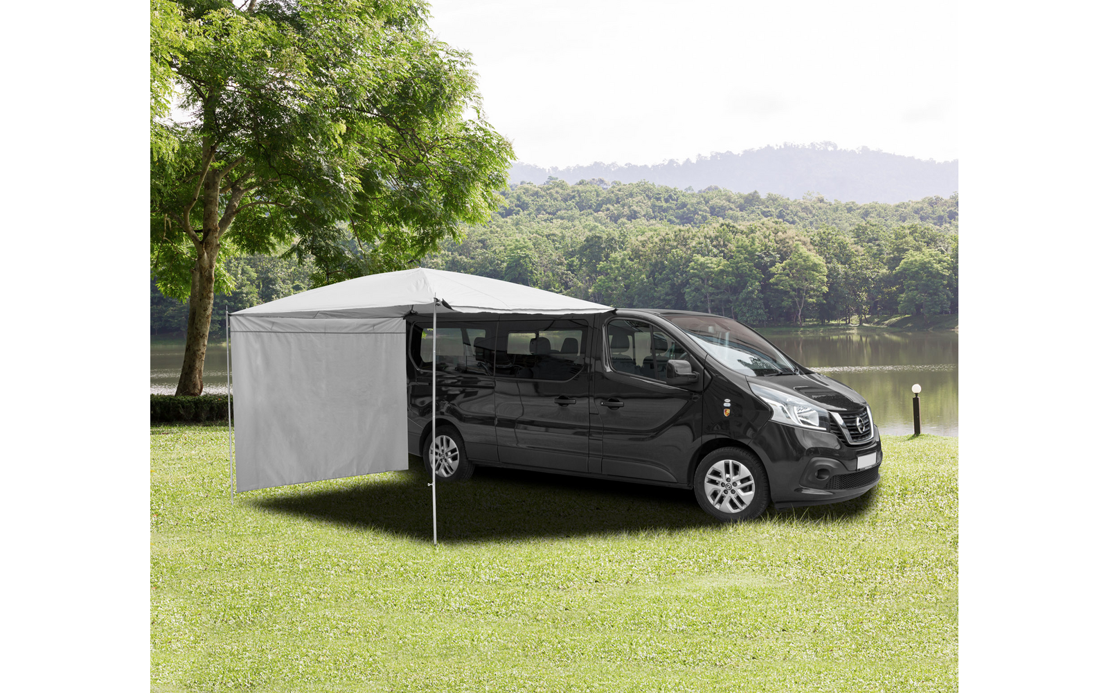 Schwarzer Transporter mit grauem Seitenschutz und Markise auf einer Wiese neben einem See