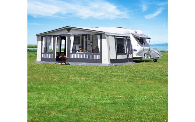 Wohnwagen mit angebauten Vorzelt auf einer grünen Wiese unter blauem Himmel
