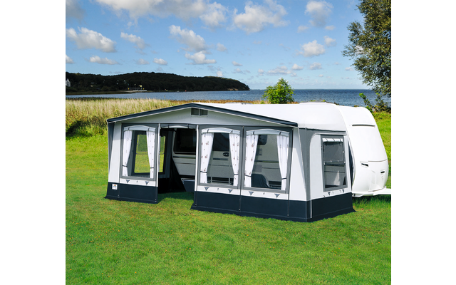 Weißes Wohnmobil mit grauem Vorzelt auf einer grünen Wiese, im Hintergrund Wasser und bewaldete Hügel