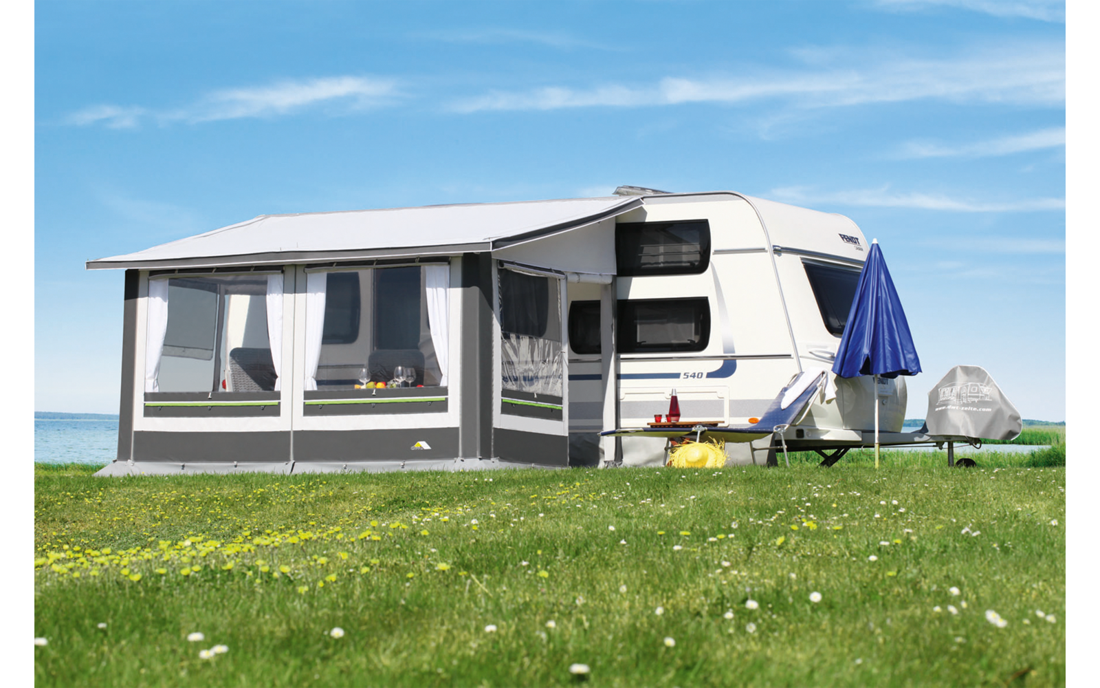 Caravan met een aanbouw op een groen grasveld onder een blauwe lucht