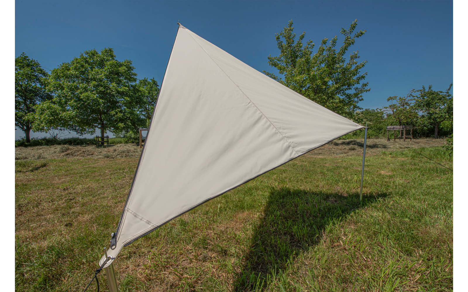 Dreieckiger Sonnensegel aus hellbeigem Stoff auf einer Wiese, gehalten von Metallstangen
