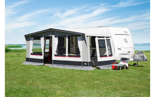 Wohnwagen mit angebautem Vorzelt auf einer grünen Wiese bei blauem Himmel