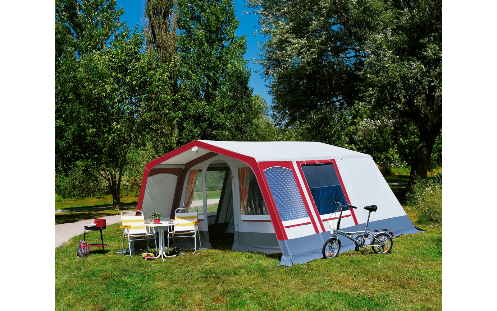 Großes Zelt mit Vorzelt auf einer grünen Wiese, zwei Fahrräder davor, sonniger Tag mit blauem Himmel