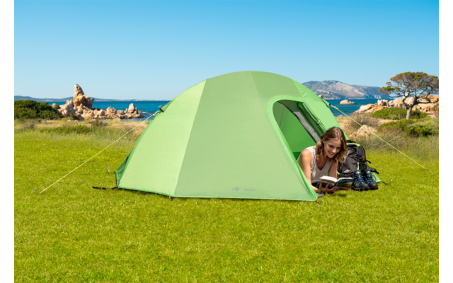 Grünes Zelt auf einer Wiese mit einer liegenden Frau, die liest, im Hintergrund Berge und blauer Himmel