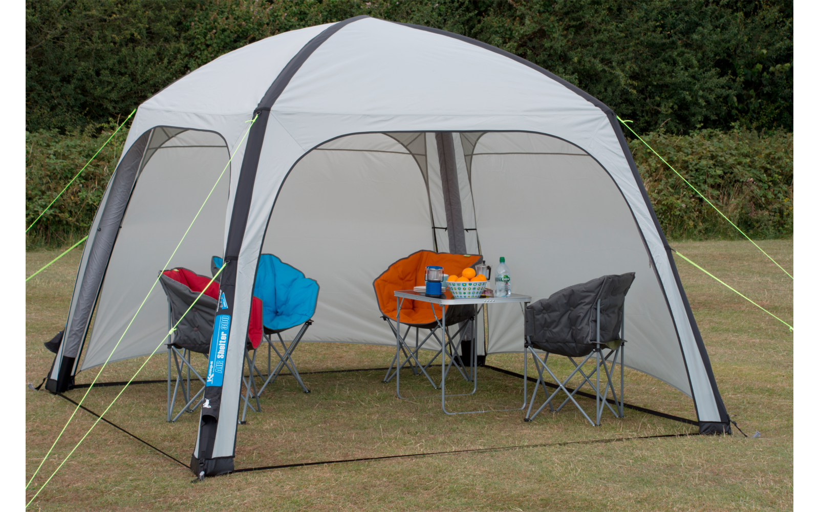 Ein Zelt mit drei Stühlen und einem Tisch mit verschiedenen Gegenständen darauf, im Freien auf einer Wiese