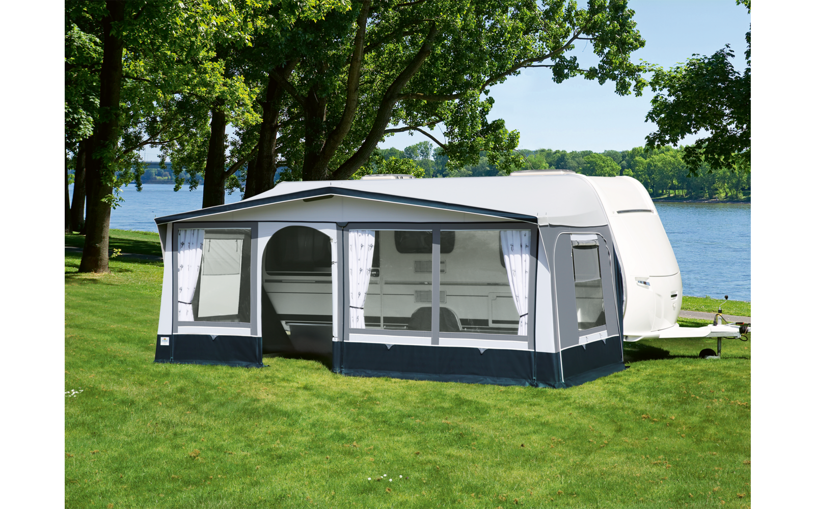 Wohnwagen mit angebautem Vorzelt auf einer Wiese neben einem See