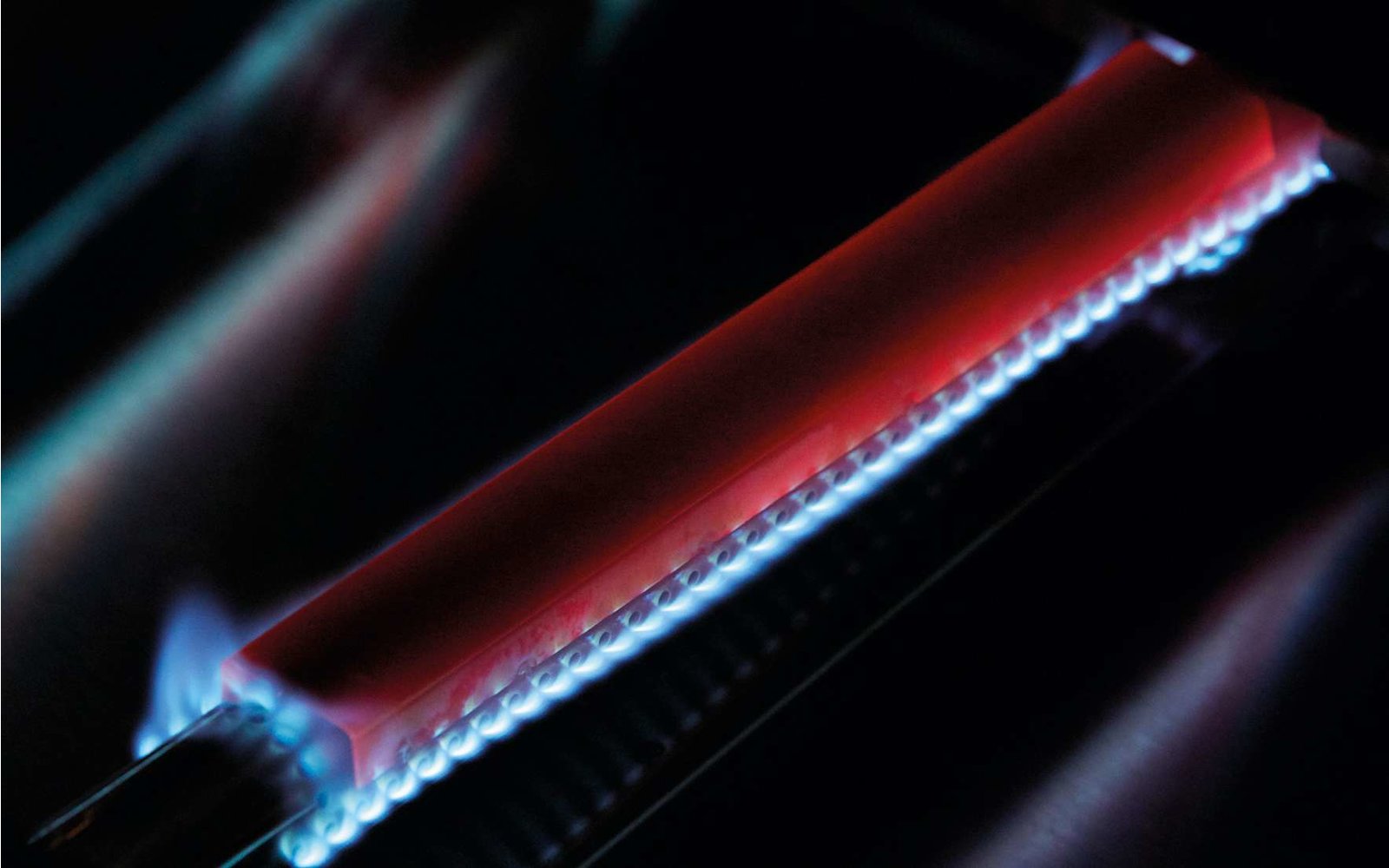 Nahaufnahme einer rot leuchtenden Heizspirale mit blauer Flamme