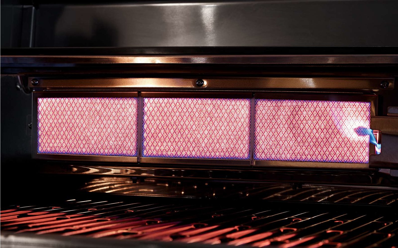 Nahaufnahme eines eingeschalteten Gasgrills mit sichtbaren Flammen und Brennern