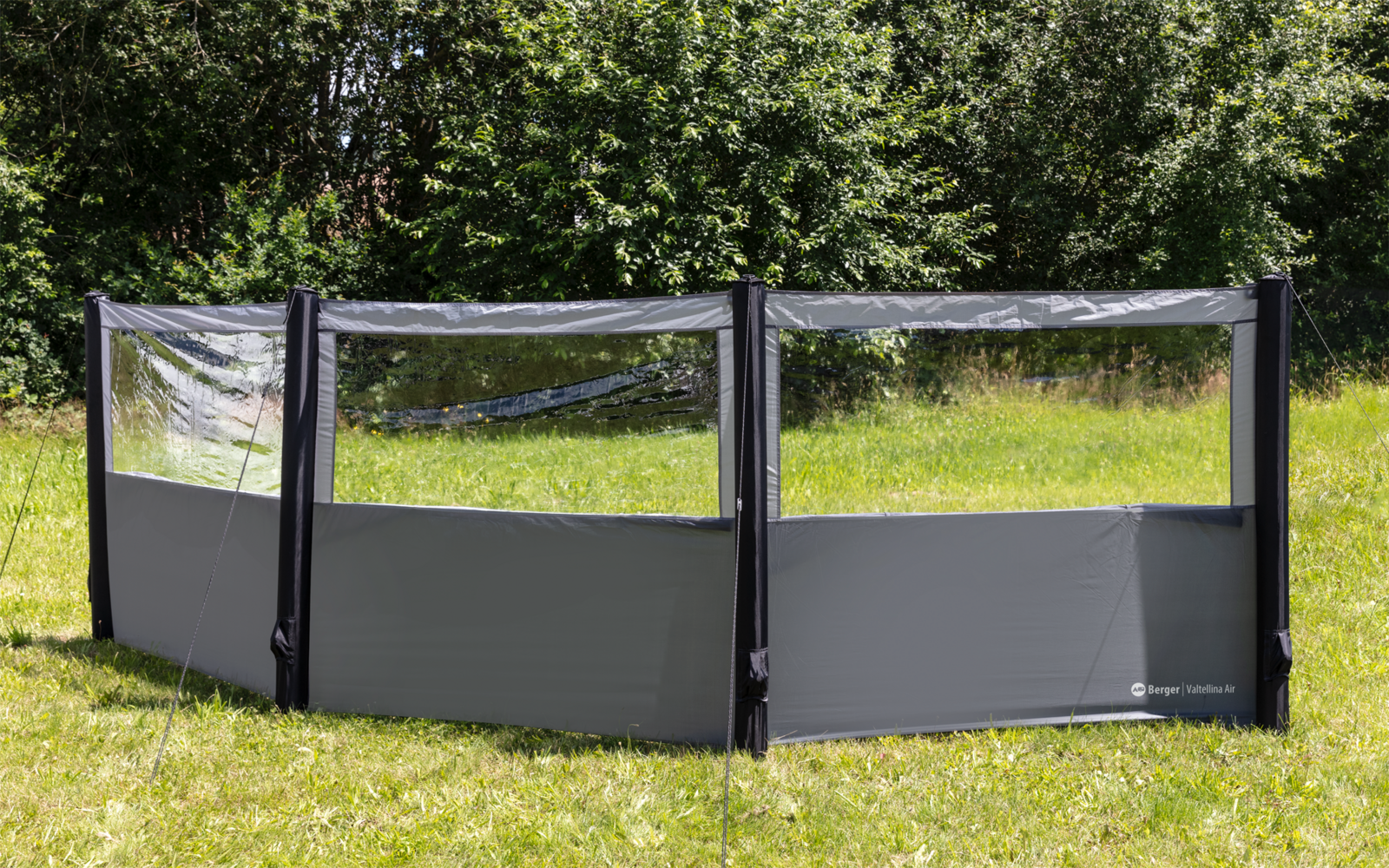 Schwarzer dreiteiliger Windschutz auf einer Wiese vor Bäumen