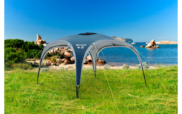 Graues Zelt auf grüner Wiese mit klarem blauen Himmel und Felsen im Hintergrund am Meer