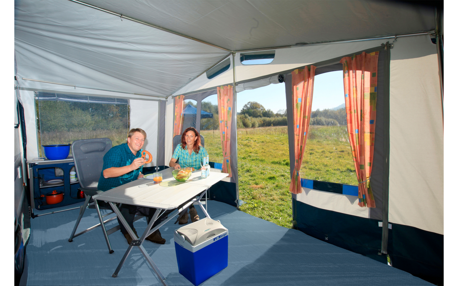 Interior view of a tent with camping table, chairs, and view of a green meadow