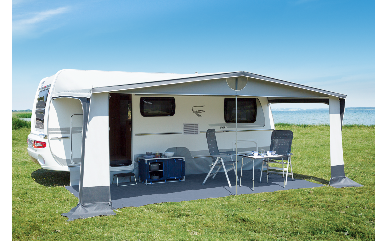 Camper van on a green meadow, with an extended awning and a table with chairs underneath