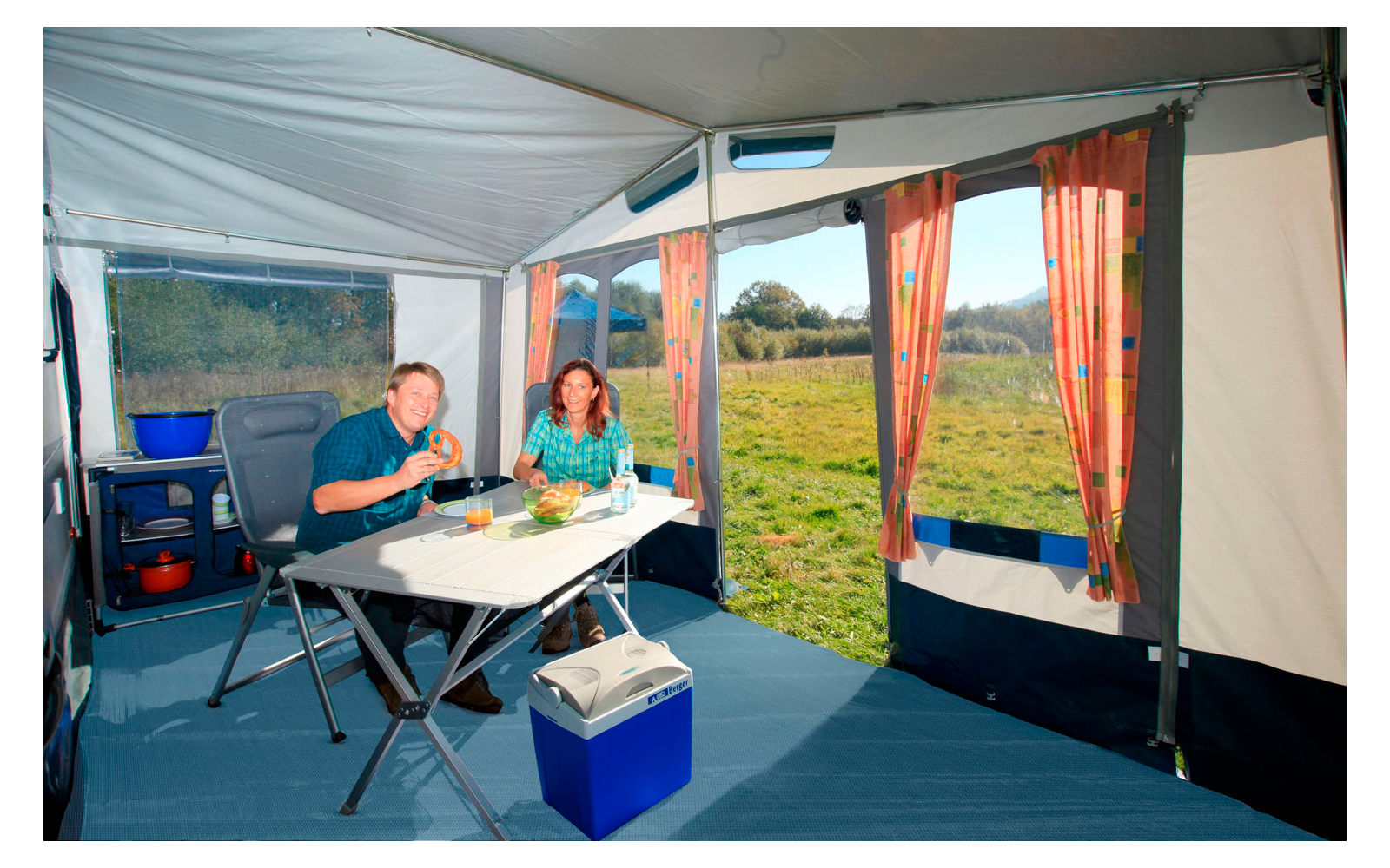 Interior view of a tent with camping table, chairs, and view of a green meadow