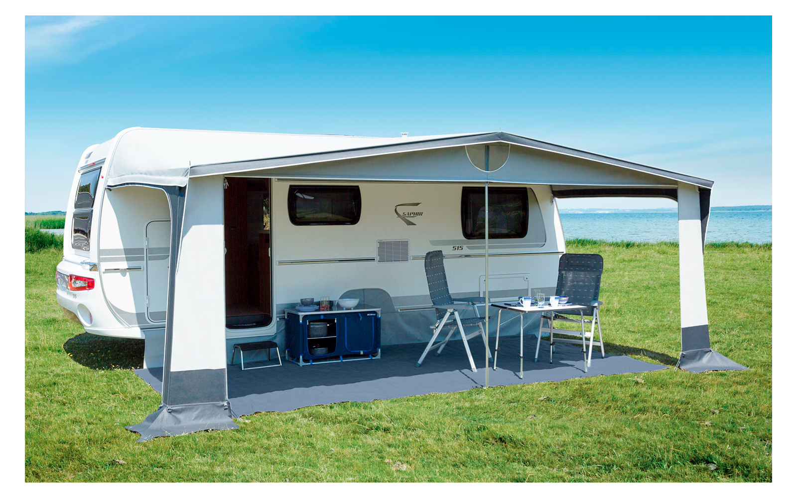 Camper van on a green meadow, with an extended awning and a table with chairs underneath