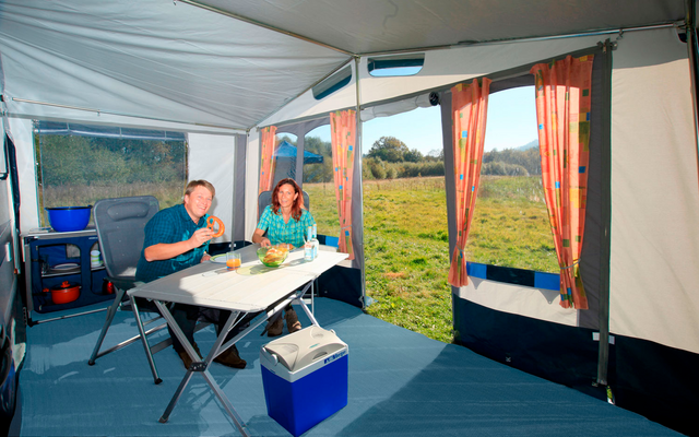 Interior view of a tent with camping table, chairs, and view of a green meadow