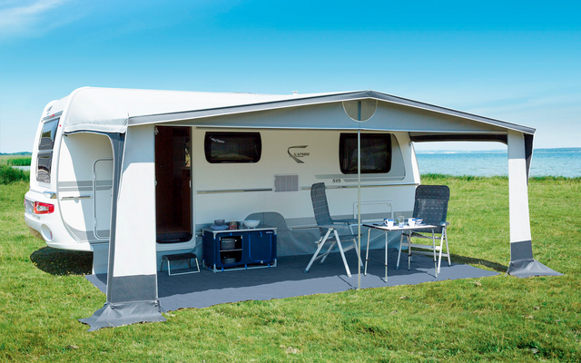 Camper van on a green meadow, with an extended awning and a table with chairs underneath
