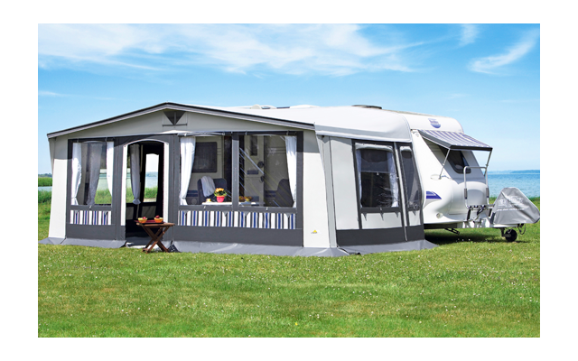 Wohnwagen mit angebauten Vorzelt auf einer grünen Wiese unter blauem Himmel