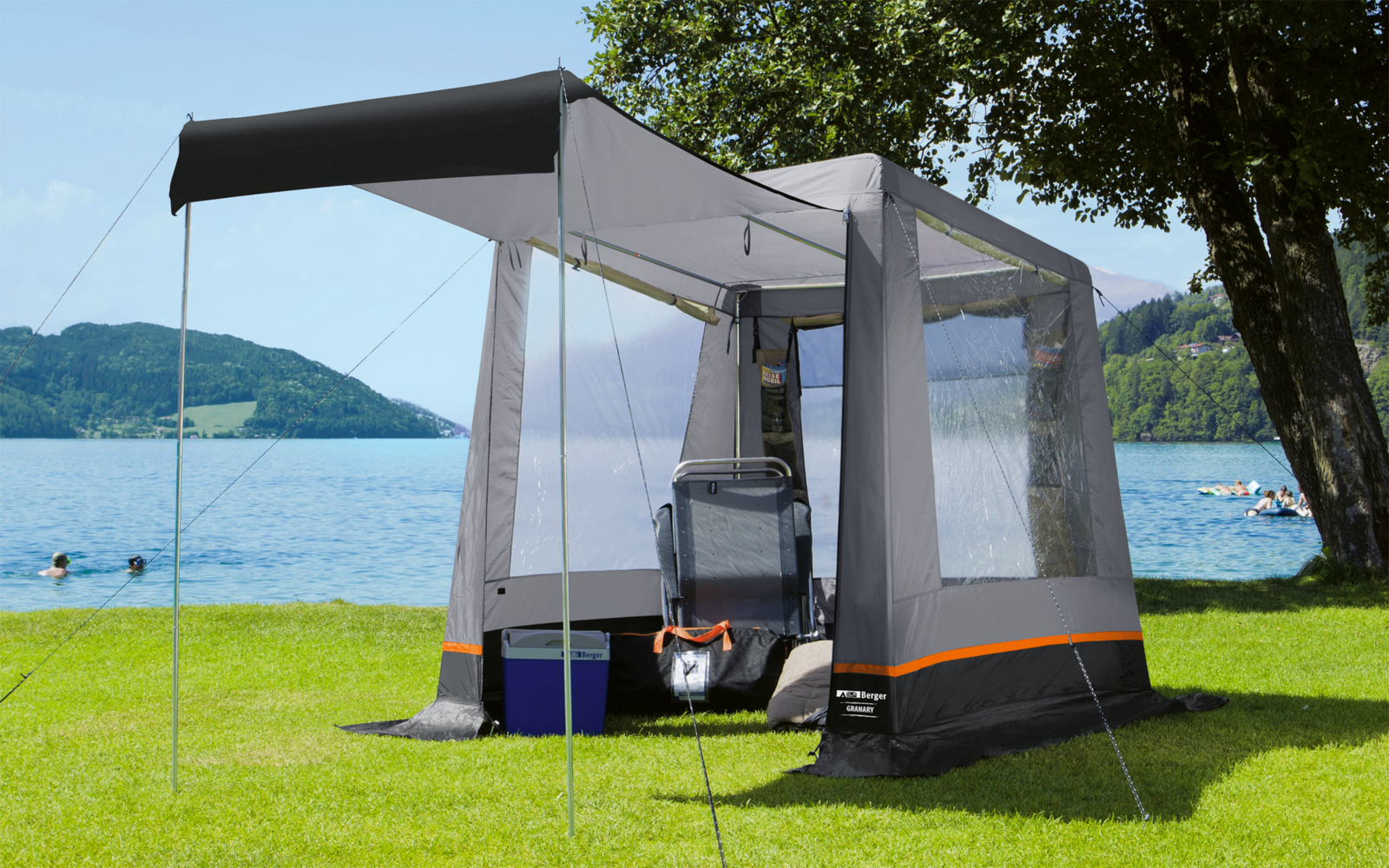 Tente avec moustiquaire sur une pelouse verte au bord d'un lac, montagnes et ciel bleu en arrière-plan