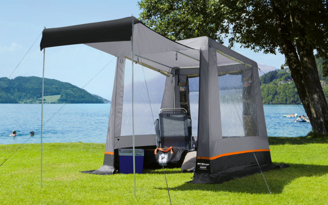 Tente avec moustiquaire sur une pelouse verte au bord d'un lac, montagnes et ciel bleu en arrière-plan