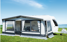 Caravan with attached awning on a green meadow under a blue sky