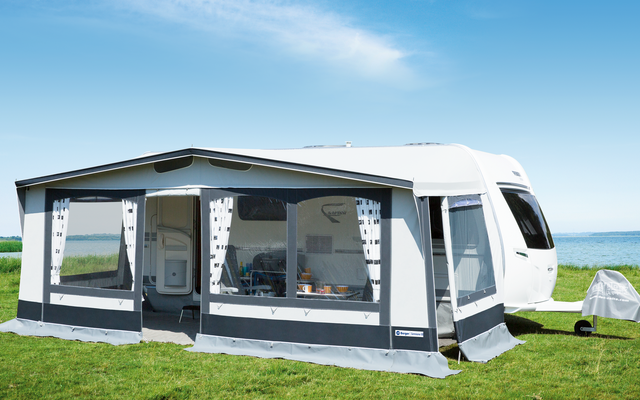 Wohnwagen mit angebautem Vorzelt auf einer grünen Wiese unter blauem Himmel