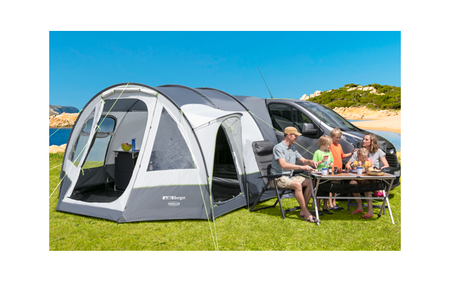 Familia sentada en una mesa de camping frente a una autocaravana blanca con una tienda adjunta