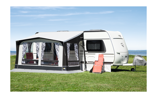 Caravana con toldo adjunto en un césped junto a un lago