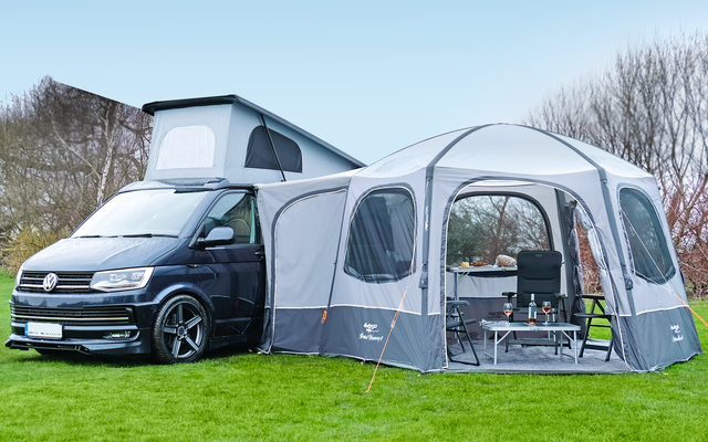 Schwarzer Campingbus mit aufgestelltem Dach und grauem Vorzelt auf einer Wiese