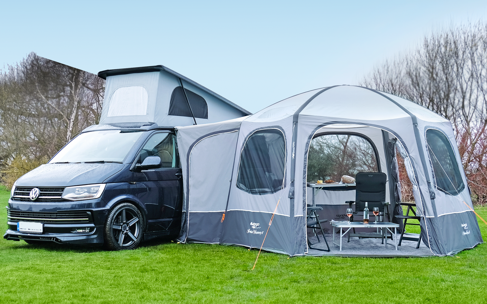 Schwarzer Campingbus mit aufgestelltem Dach und grauem Vorzelt auf einer Wiese