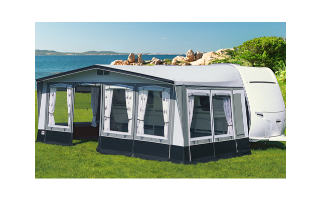 Ein großes, graues Campingzelt mit Fenstern steht auf einer grünen Wiese neben einem weißen Wohnwagen