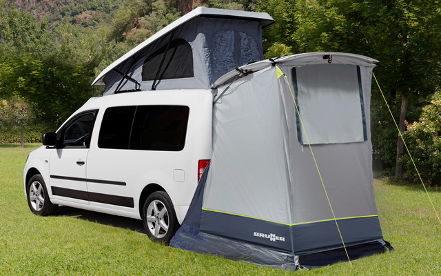 Witte bus met opgezet tentaanhangsel op een groen weiland voor beboste bergen