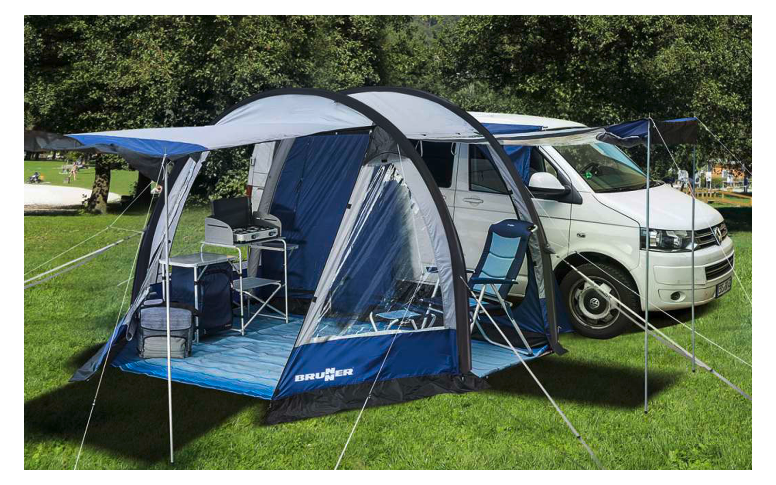 Campingzelt mit aufgespanntem Vordach neben weißem Wohnmobil auf grüner Wiese