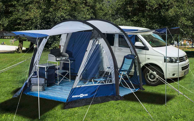 Campingzelt mit aufgespanntem Vordach neben weißem Wohnmobil auf grüner Wiese