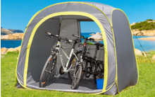 Deux vélos dans une tente grise sur une pelouse au bord de la mer