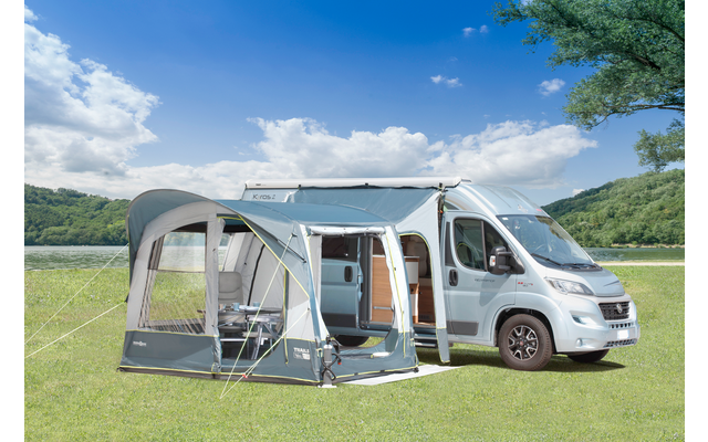Großer Wohnwagen mit Markise, davor zwei Campingstühle und ein Tisch, auf grüner Wiese bei sonnigem Himmel
