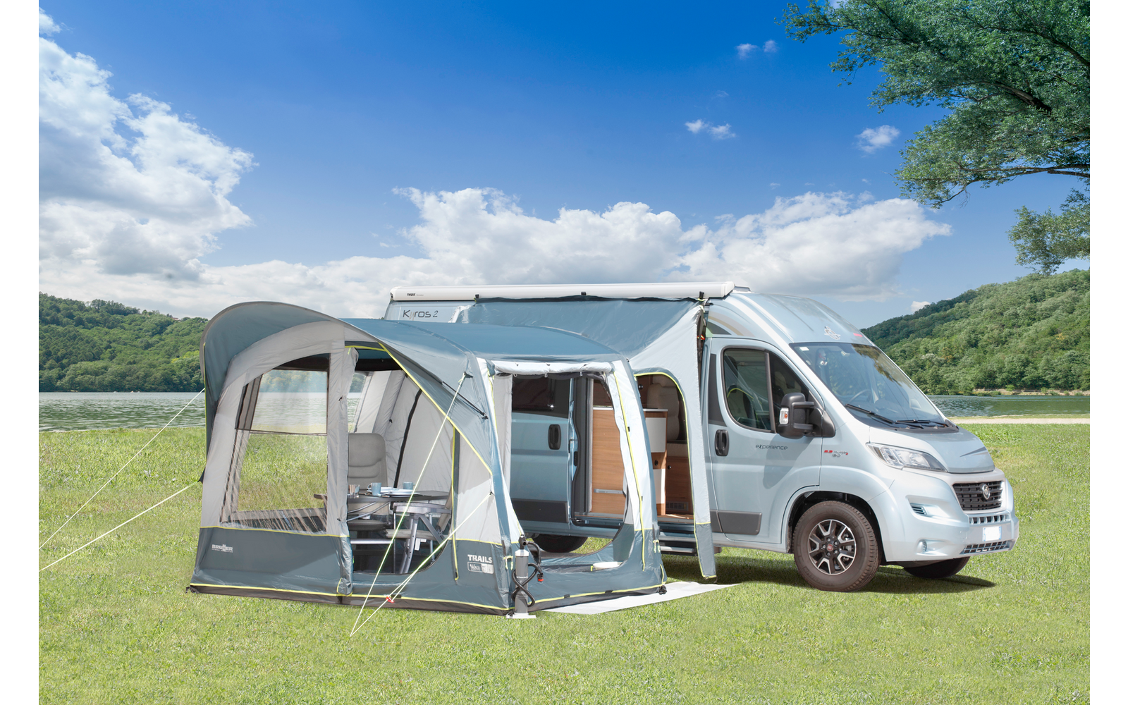 Großer Wohnwagen mit Markise, davor zwei Campingstühle und ein Tisch, auf grüner Wiese bei sonnigem Himmel