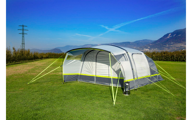 Großes, helles Zelt steht auf grünem Rasen, Berge im Hintergrund unter blauem Himmel