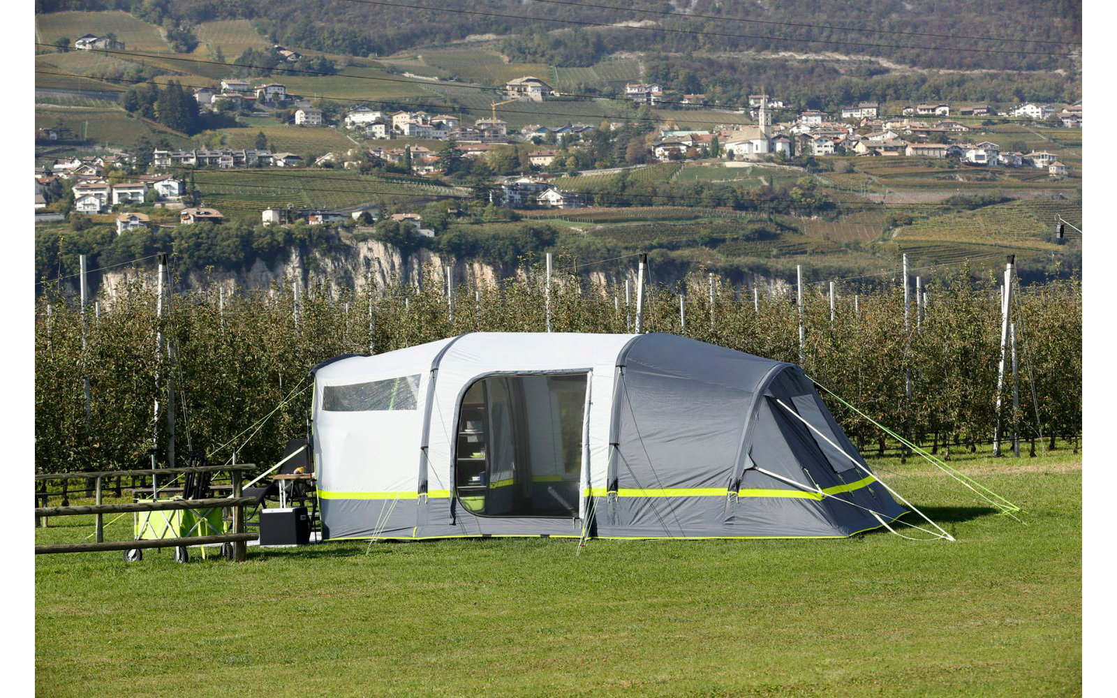 Wohnwagen mit Vorzelt steht auf einer grünen Wiese, im Hintergrund Hügel und Bäume
