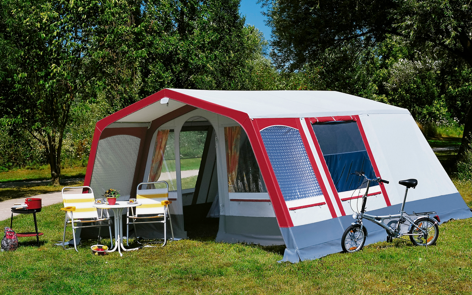 Grote tent met voortent op een groen grasveld, twee fietsen ervoor, zonnige dag met blauwe lucht