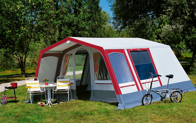 Grote tent met voortent op een groen grasveld, twee fietsen ervoor, zonnige dag met blauwe lucht