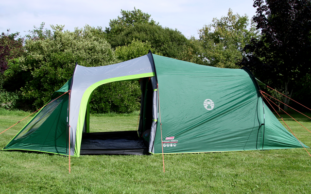 Groene tent met open ingang op een grasveld, omgeven door bomen