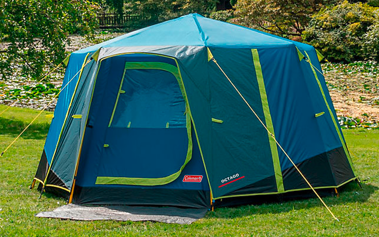 Blue camping tent standing on a green lawn with trees in the background