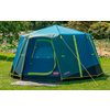 Blue camping tent standing on a green lawn with trees in the background