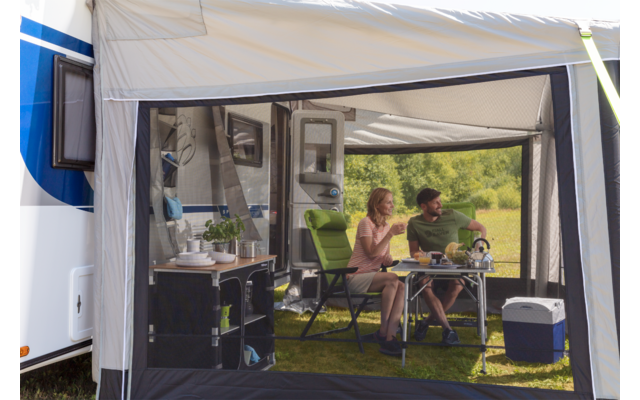 Zwei Personen sitzen an einem Tisch in einem Zelt vor einem Wohnmobil