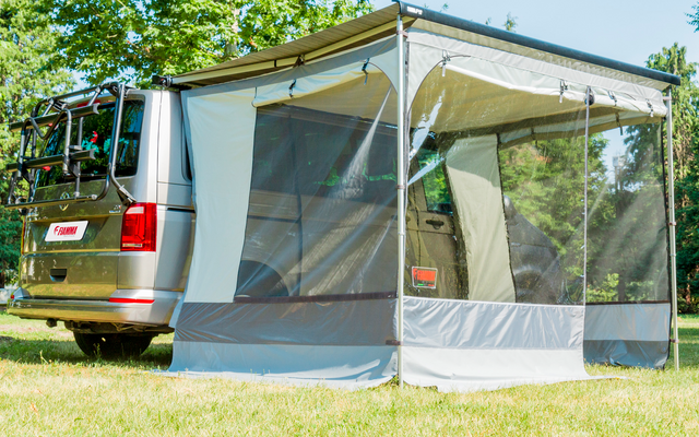 Furgone da campeggio con tenda annessa su erba verde sotto gli alberi