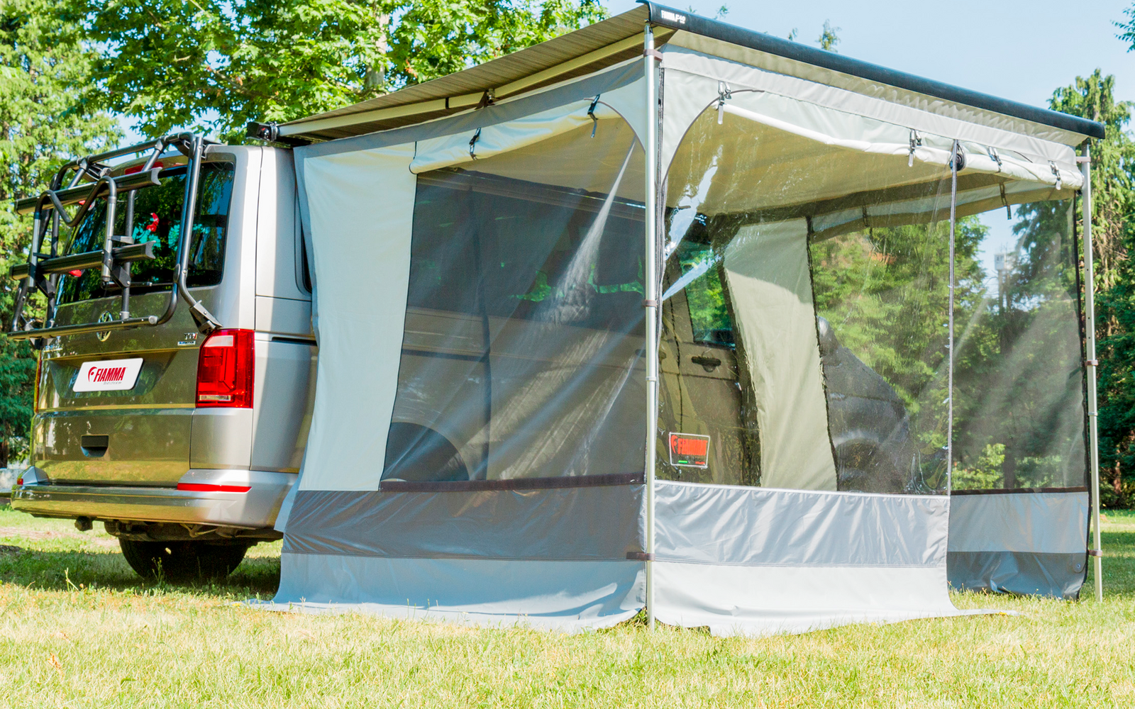 Furgone da campeggio con tenda annessa su erba verde sotto gli alberi