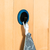 Main accrochant un tissu gris à un crochet mural bleu sur une porte en bois