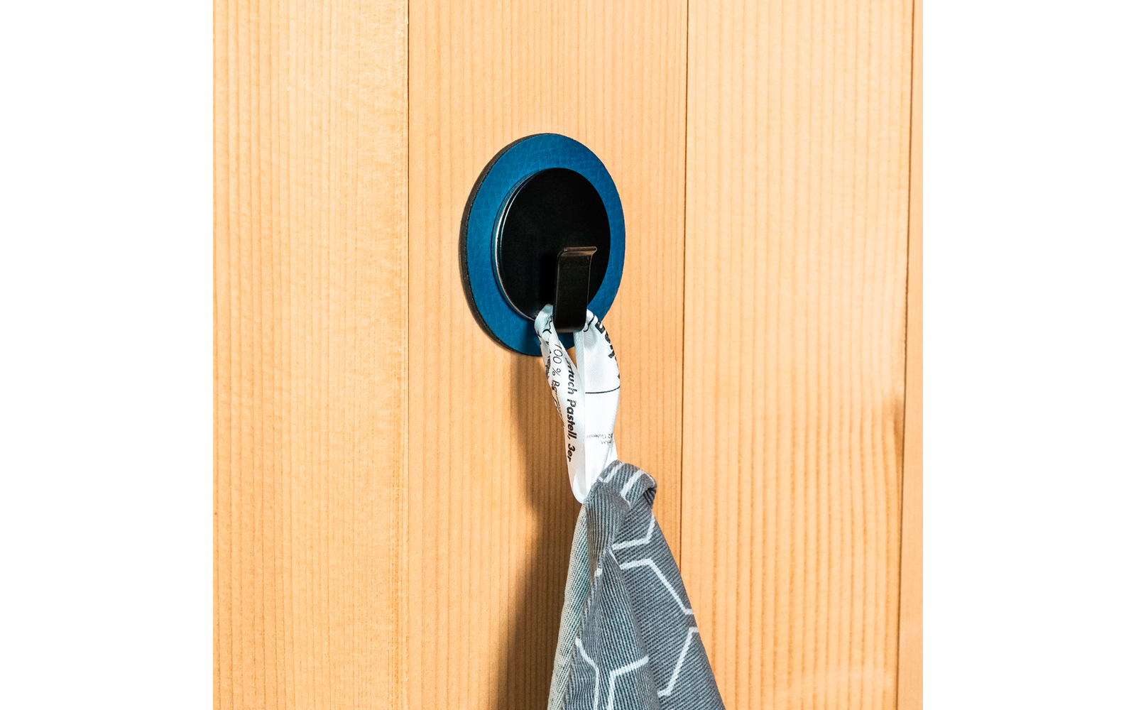 Main accrochant un tissu gris à un crochet mural bleu sur une porte en bois