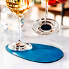 Wine glass on blue coaster with wine bottle and wine glass in the background